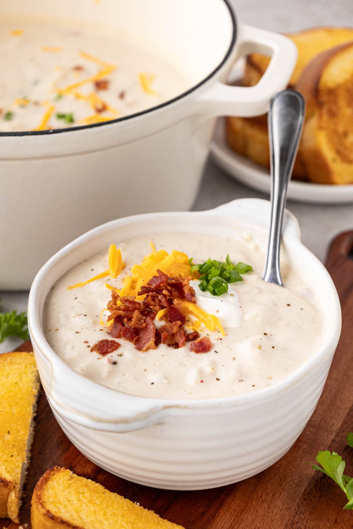 A bowl of creamy potato soup topped with a dollop of sour cream, bacon and cheese.