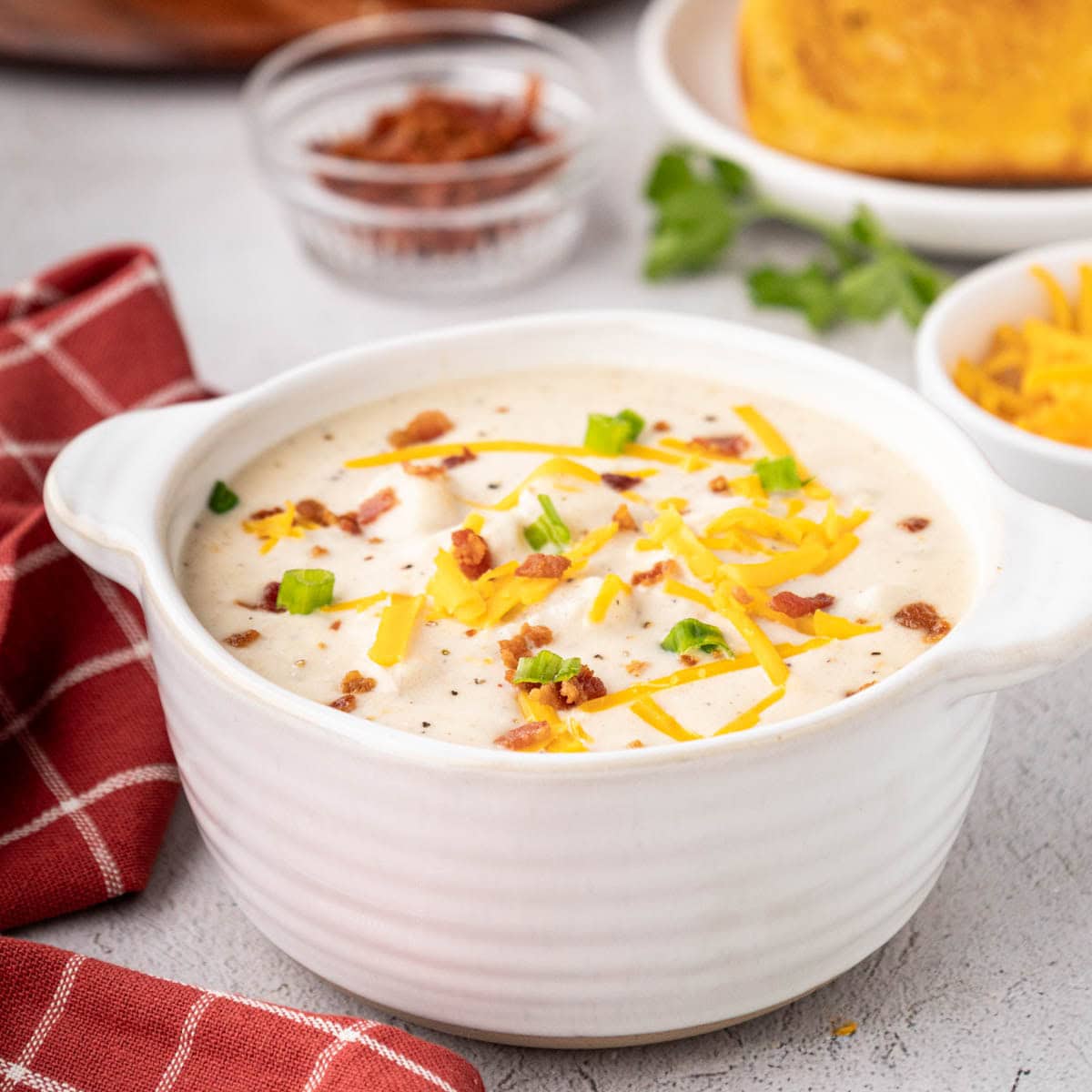 Bowl of creamy potato soup garnished with shredded cheese, bacon, and chives.