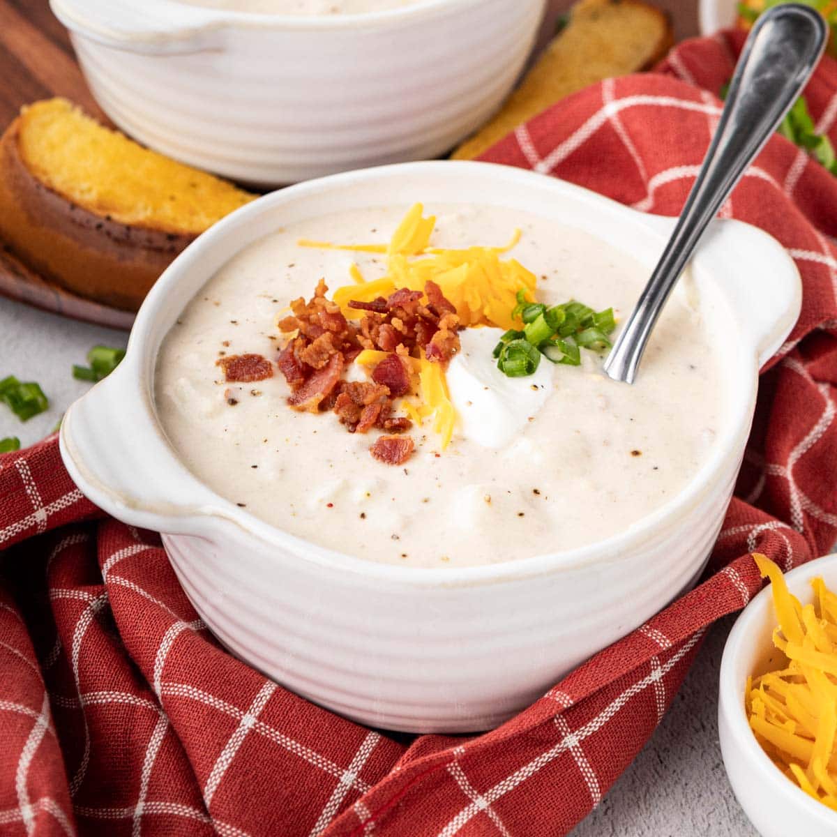 Bowl of potato soup set on a red and white check napkin.
