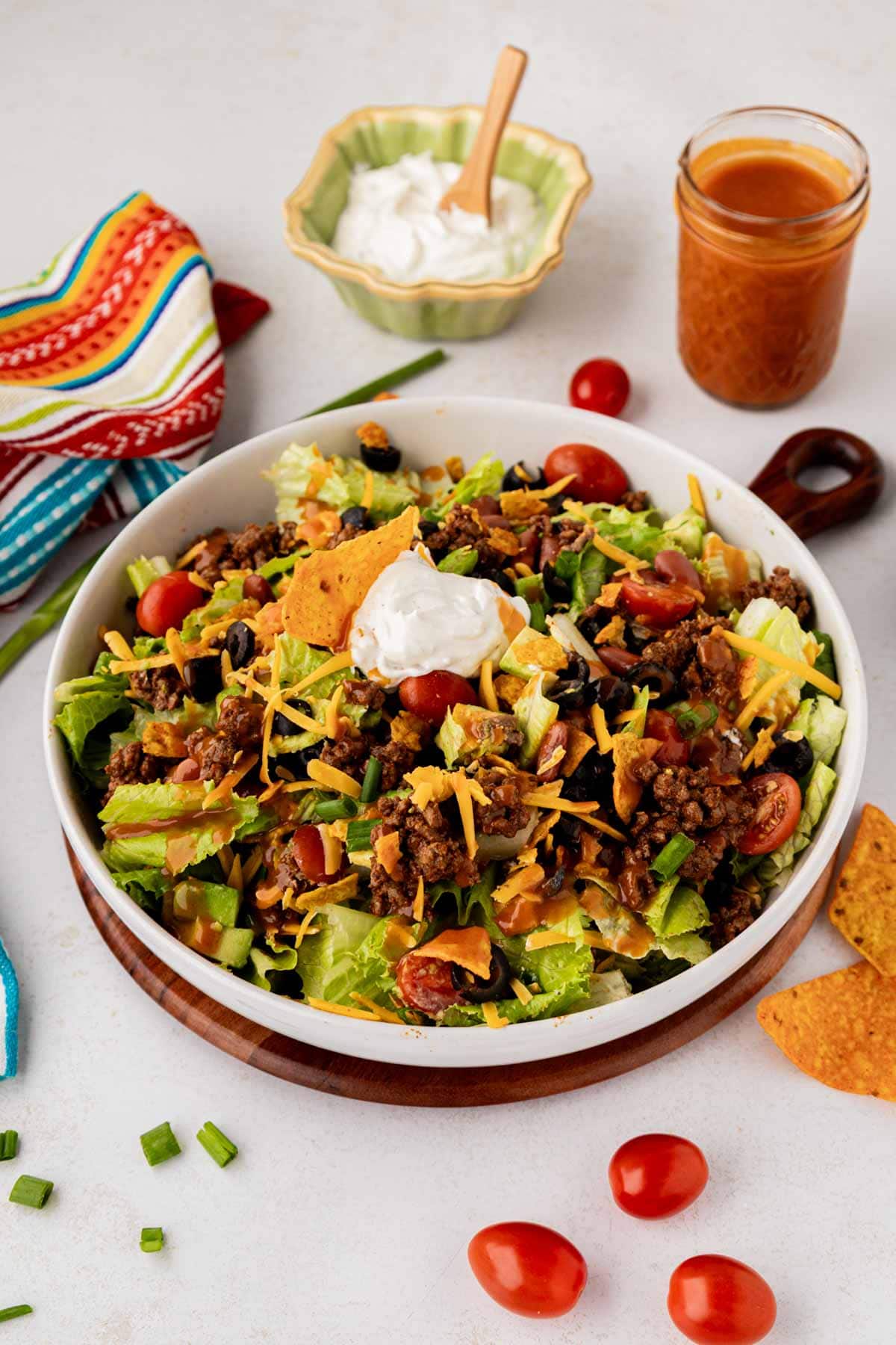 A white salad serving bowl with a taco salad with Doritos and Catalina dressing.