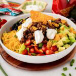 A white salad serving bowl with a taco salad with Doritos and Catalina dressing.