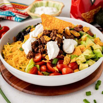 A white salad serving bowl with a taco salad with Doritos and Catalina dressing.