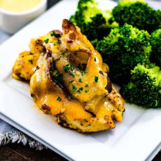 Alice Springs Chicken - a flavorful chicken breast topped with a honey mustard sauce, mushroom, cheese, and bacon is set on a plate with steamed brocoli.