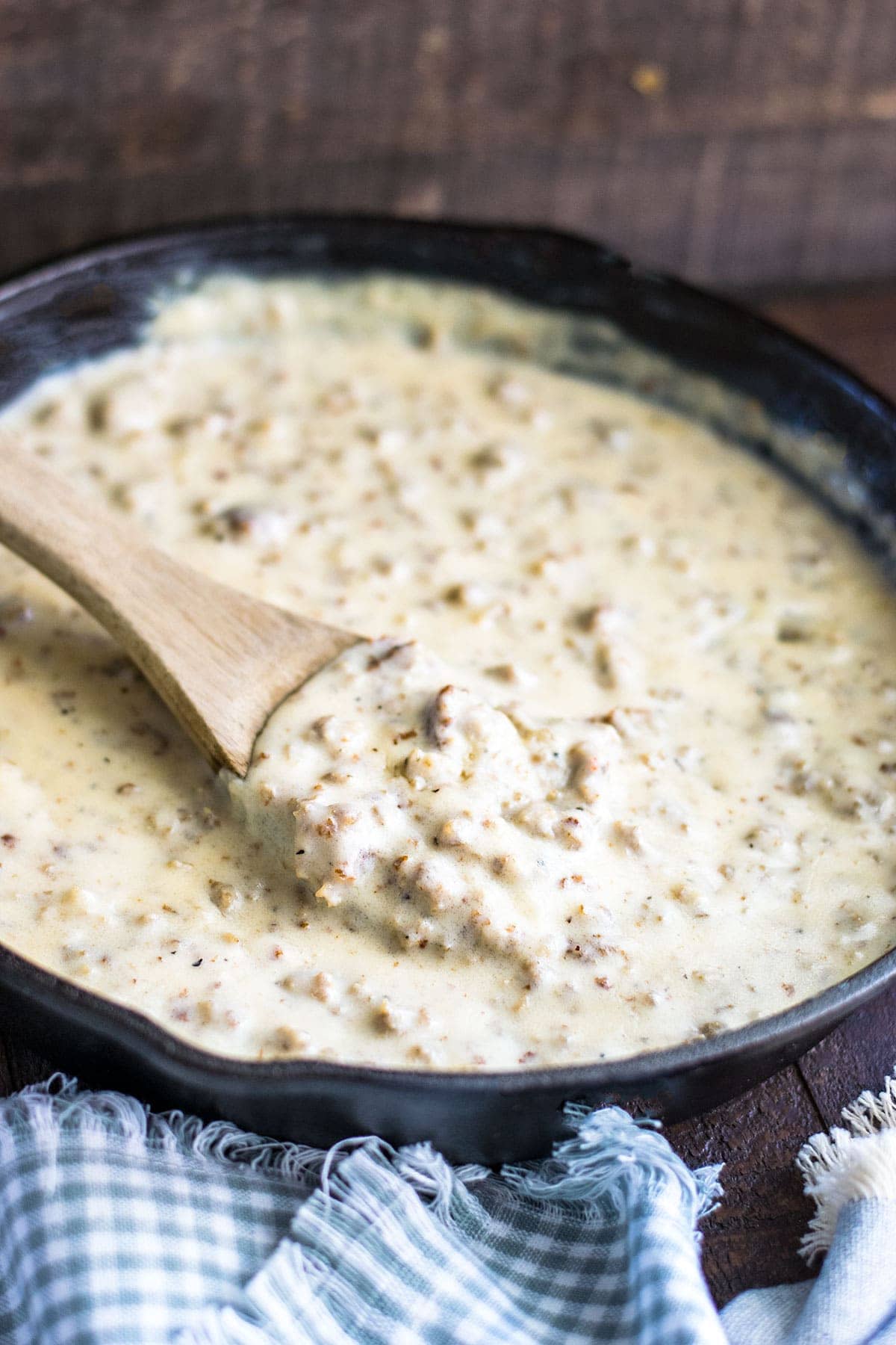 Cast iron skillet of homemade creamy sausage gravy set on a wooden tray.