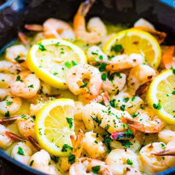 Cast iron skillet with shrimp scampi garnished with lemon slices and parsley.