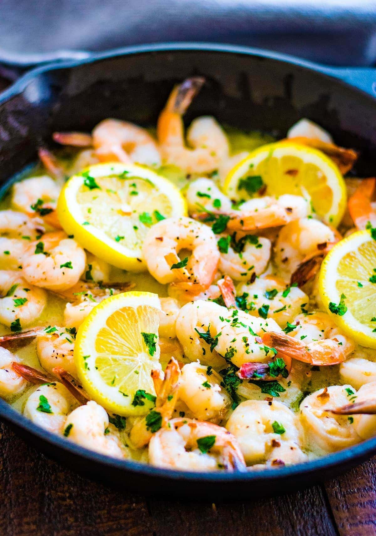 Cast iron skillet with shrimp scampi garnished with lemon slices and parsley.