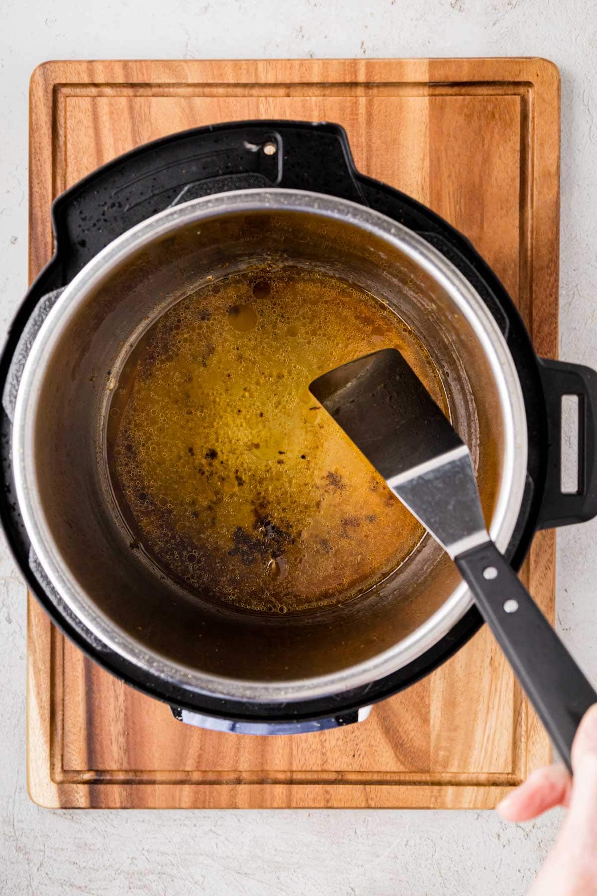Deglazing instant pot with broth and a spatula.