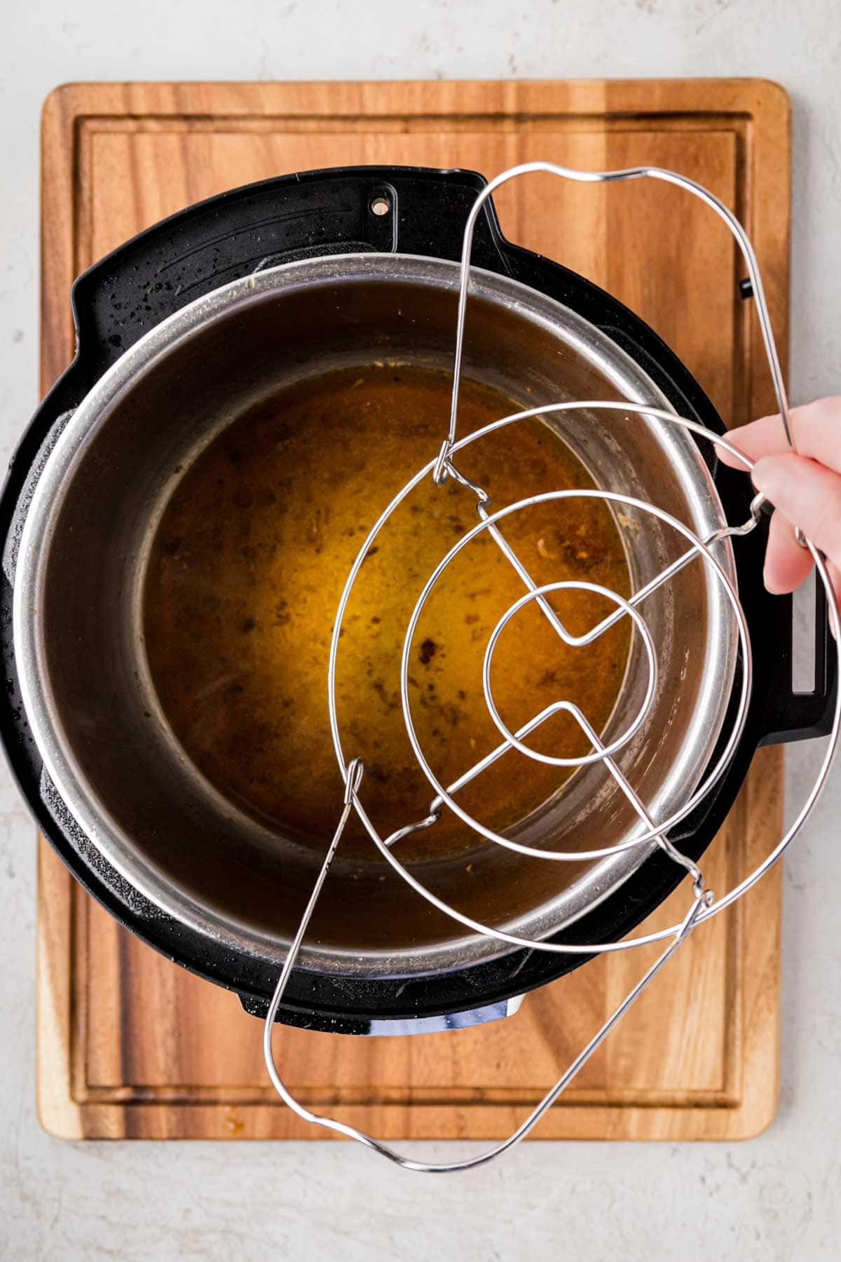 Adding trivet to the instant pot on top of the broth.