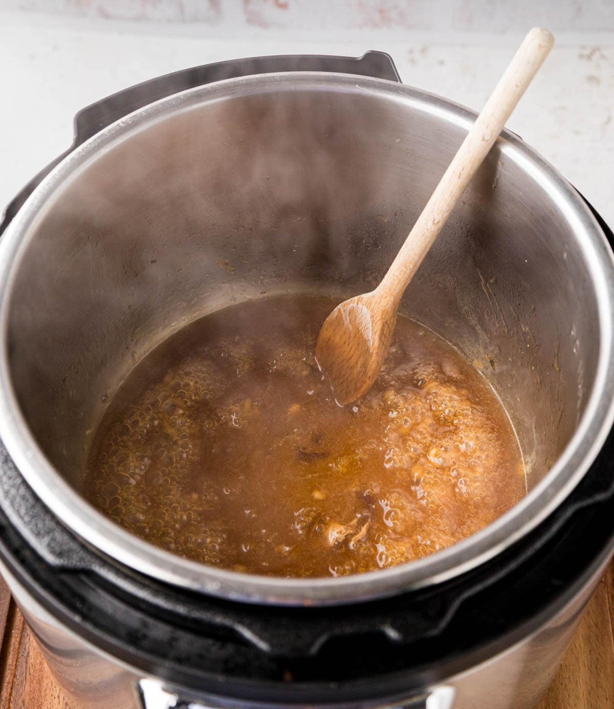 An instant pot with chicken gravy inside and a wooden spoon.