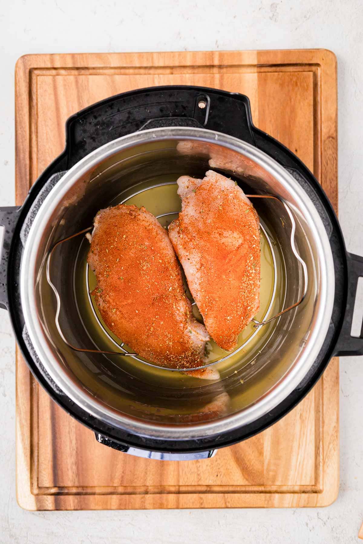 Raw seasoned chicken placed on top of trivet in the instant pot.