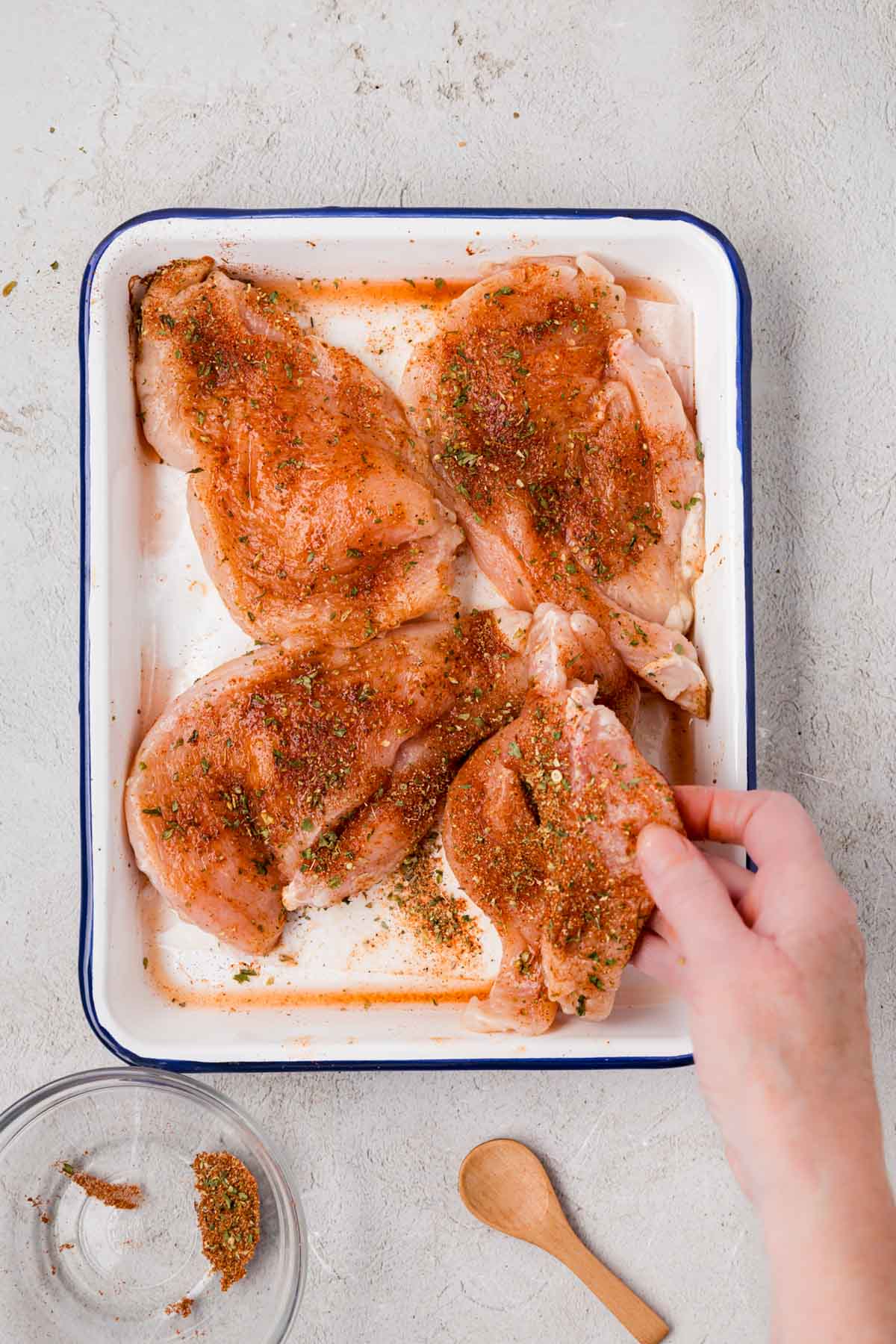 Chicken breast in a tray being seasoned.