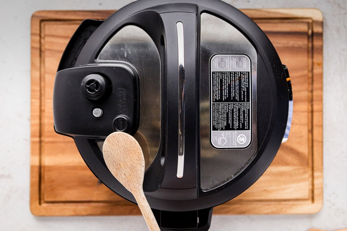 Manually releasing pressure on the instant pot by pressing the valve with a wooden spoon.