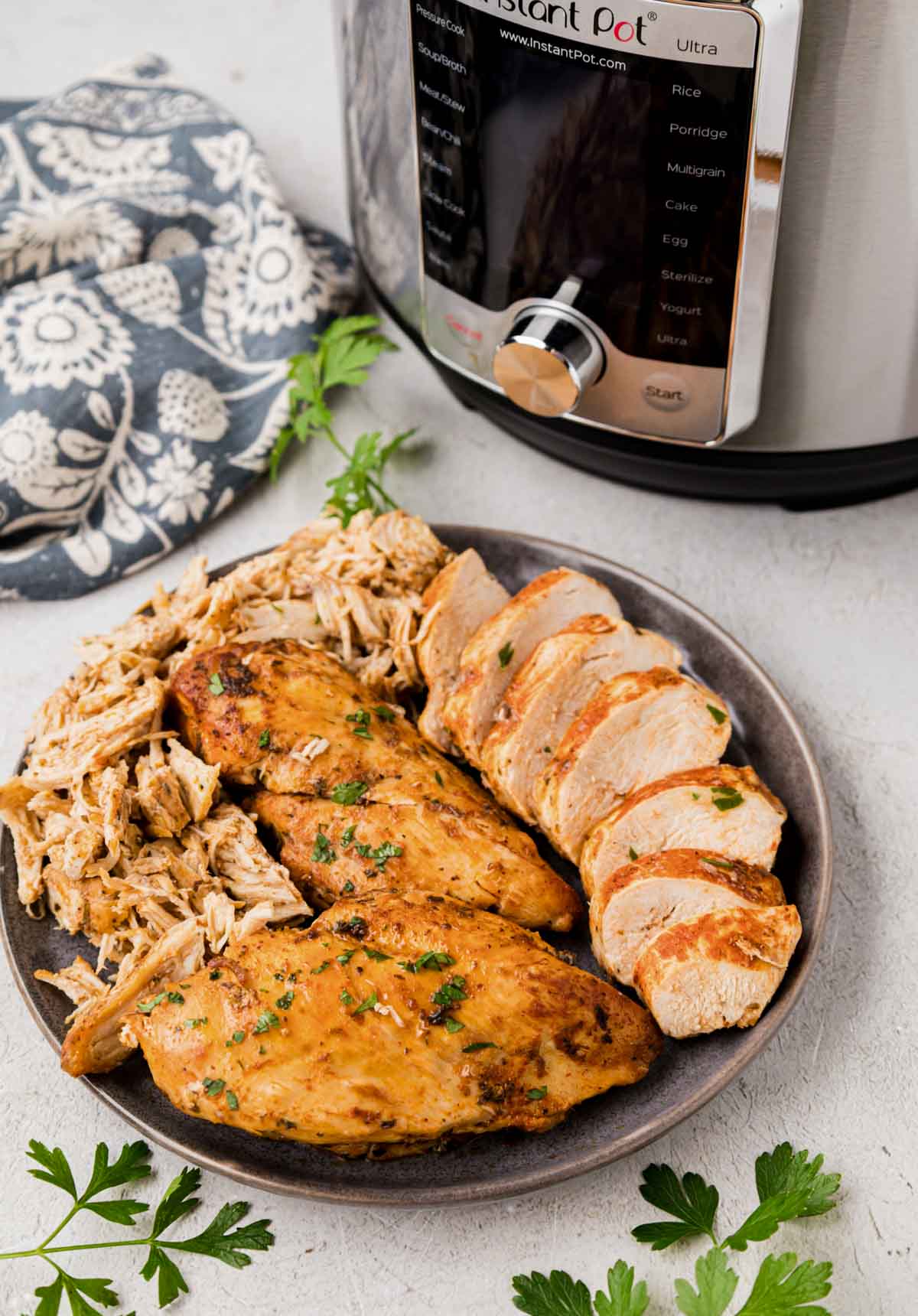 A plate with instant pot chicken breast whole, sliced and shredded with an instant pot in the background.