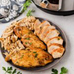 A plate with instant pot chicken breast whole, sliced and shredded with an instant pot in the background.