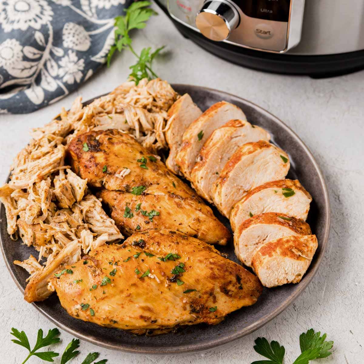 A plate with instant pot chicken breast whole, sliced and shredded with an instant pot in the background.