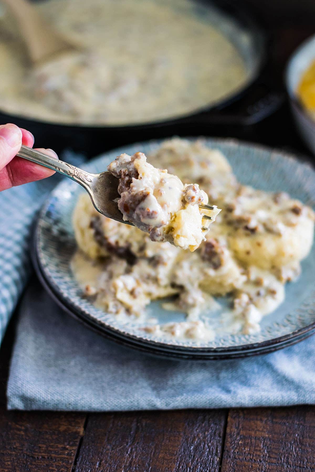 Biscuits and Gravy on a fork ready for a bite. Plated sausage gravy over biscuits in the background.