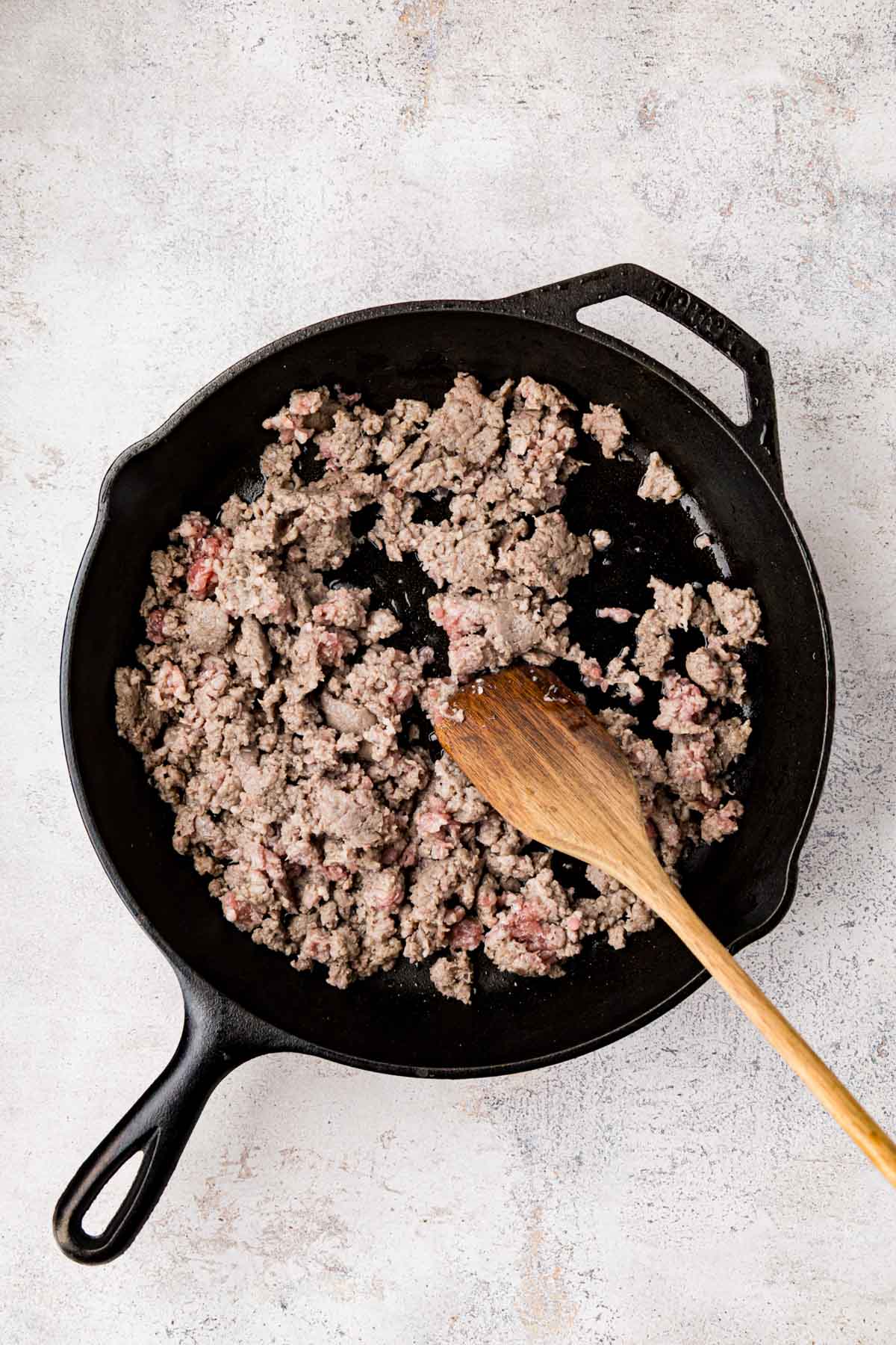 Raw breakfast sausage crumbled in a cast iron skillet.