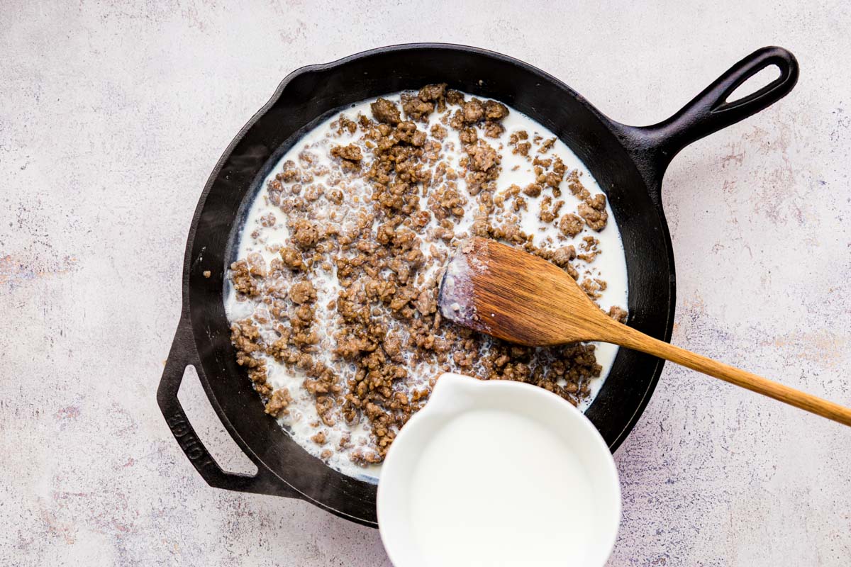 Slowly pouring whole milk into the sausage and flour roux to make sausage gravy.