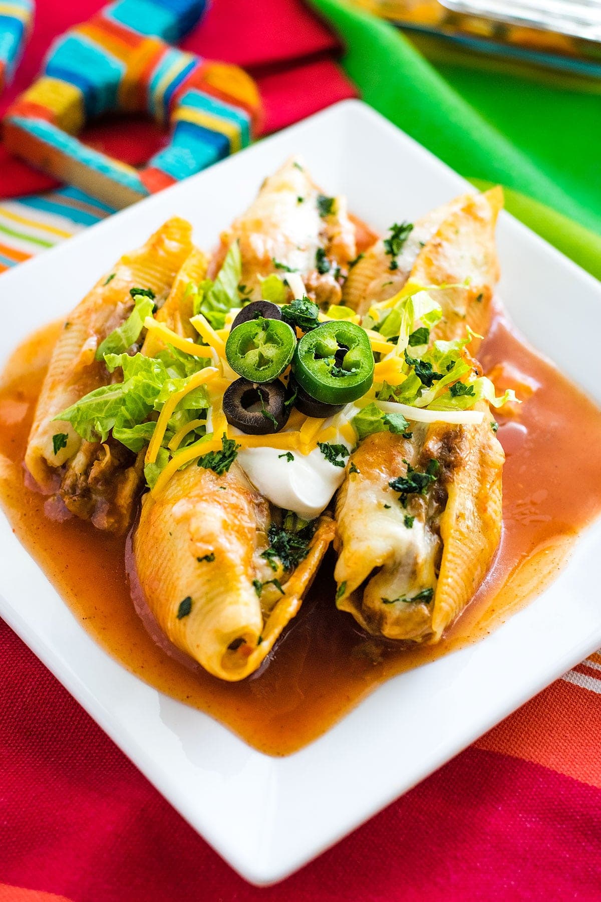 Baked Mexican Stuffed Shells topped with taco toppings on a white plate.
