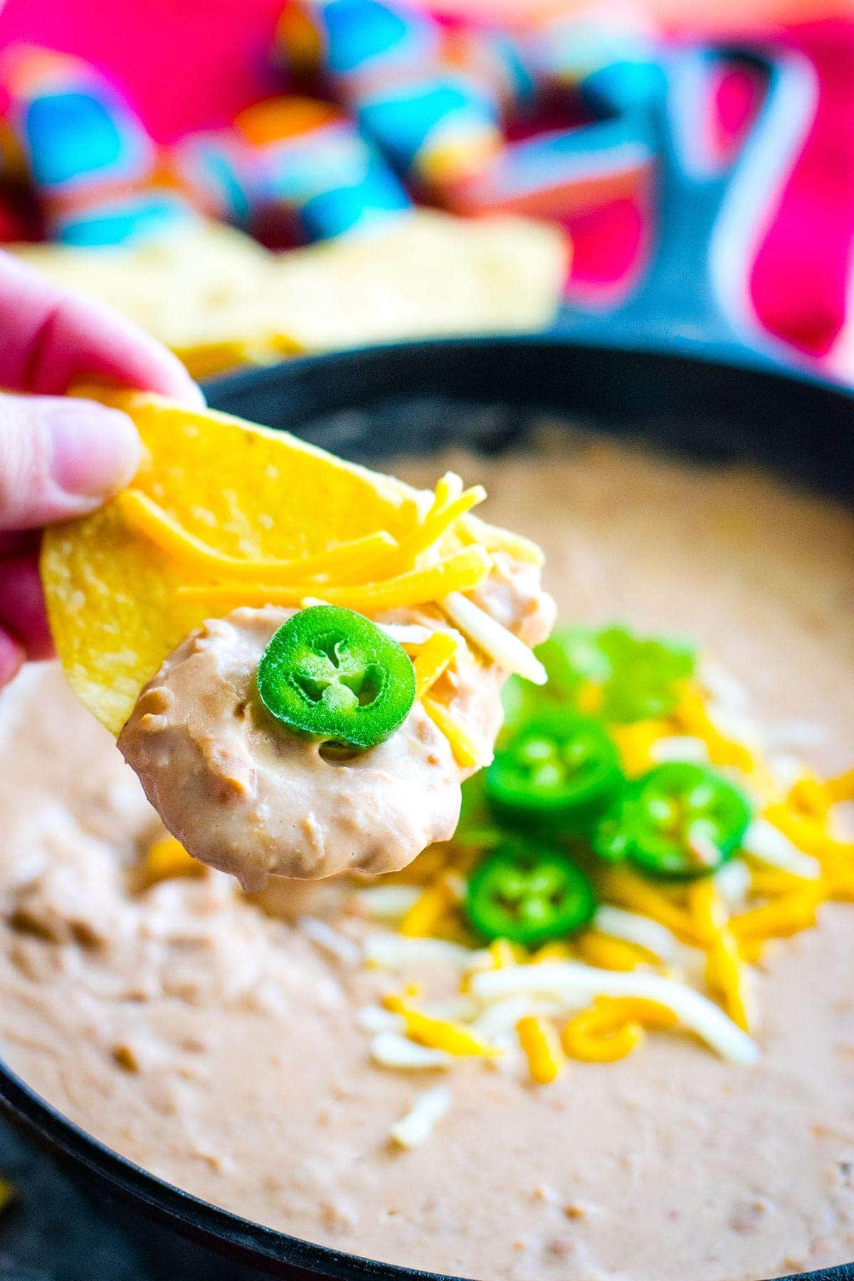 Close-up of refried beans scooped on a tortilla chip with a jalapeno.