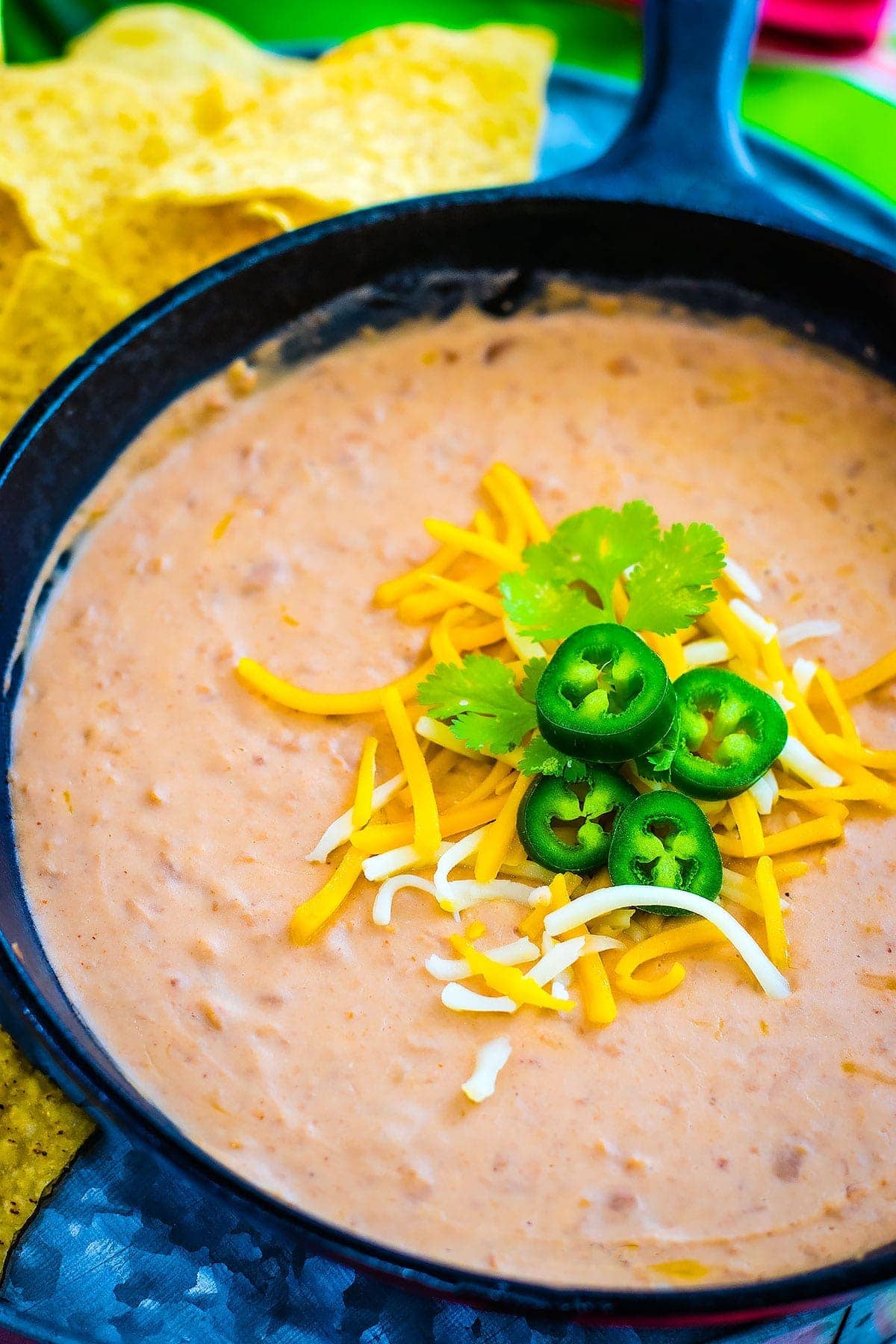 Easy Restaurant Style Refried Beans in a skillet topped with shredded cheese and jalapeno slices