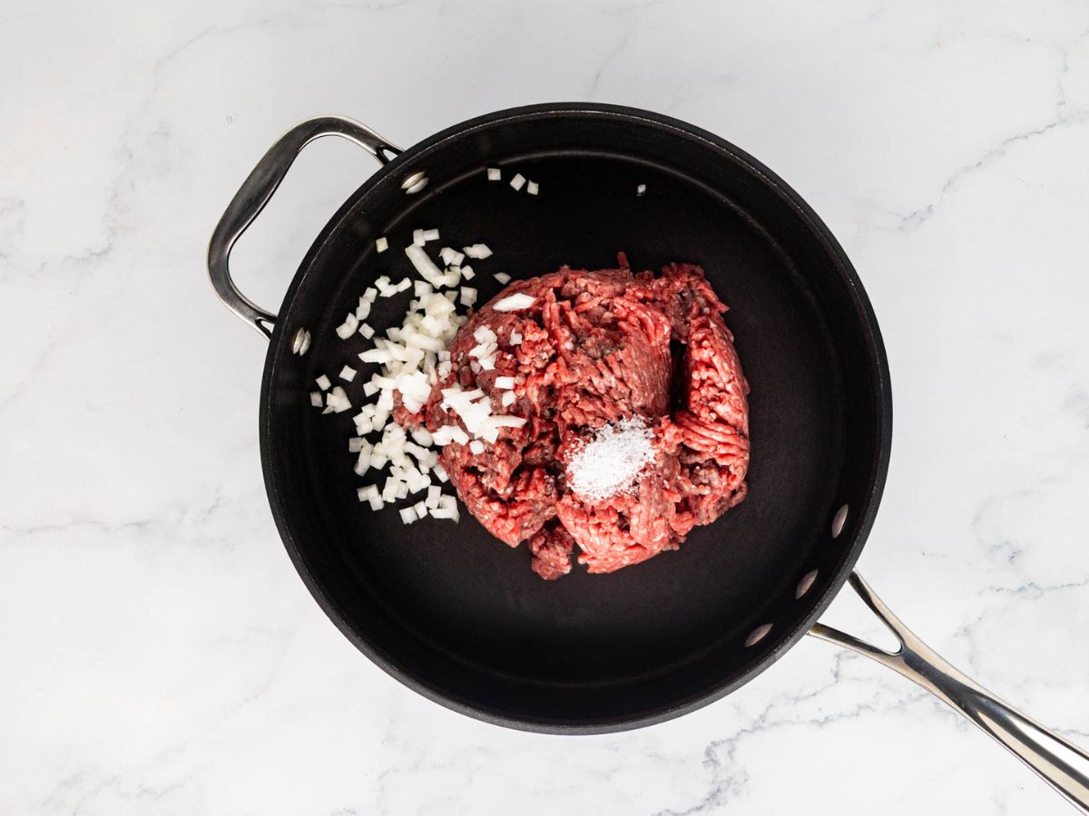Raw ground beef and onion in a skillet.