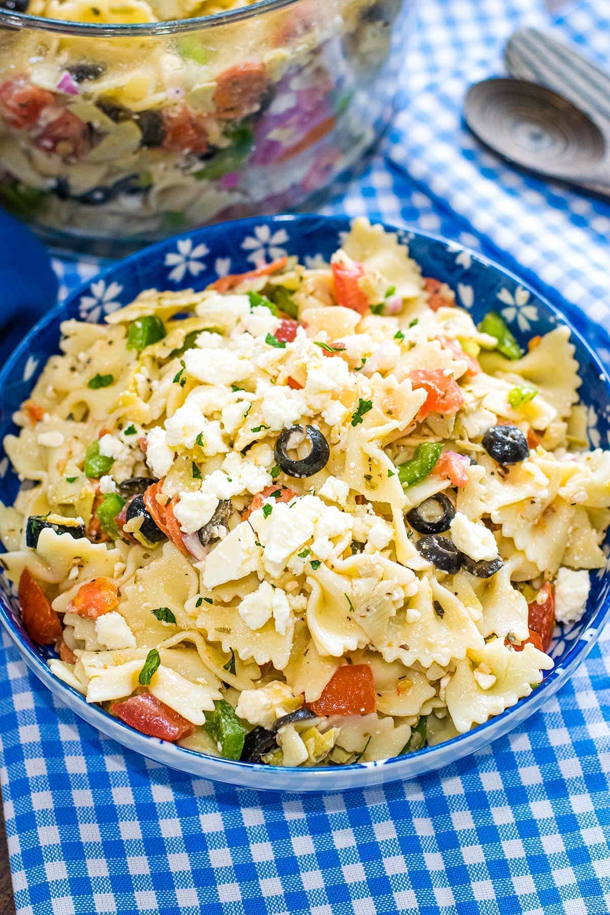 A blue bowl with Pasta salad in it on a blue checkered table setting.