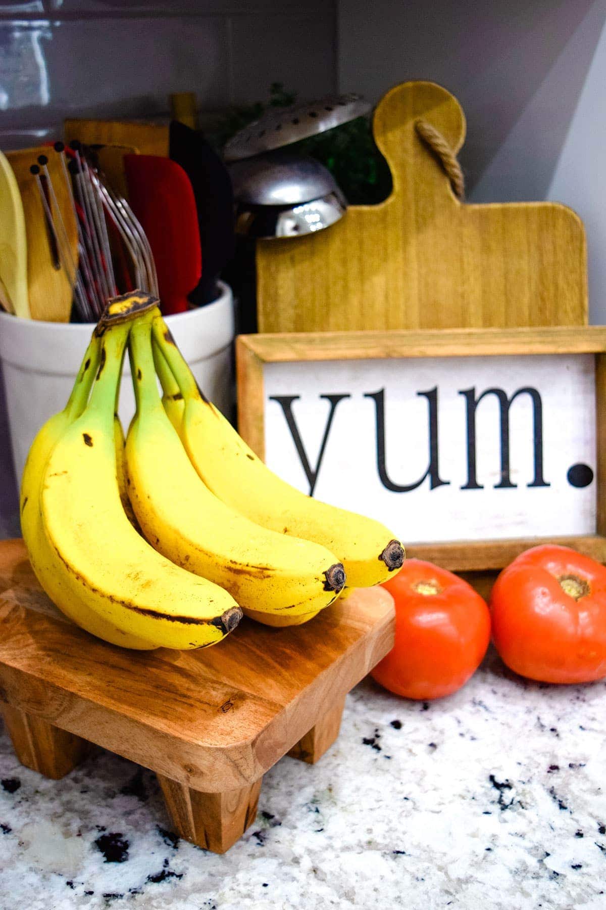 Bananas on kitchen counter with tomatoes and yum kitchen sign