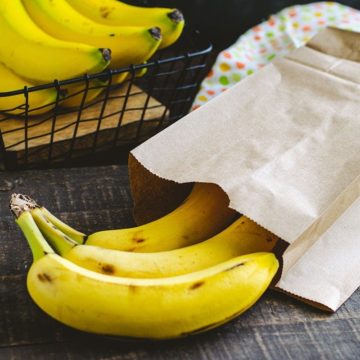 Bananas poking out of a brown paper bag sitting on top of a wooden table.