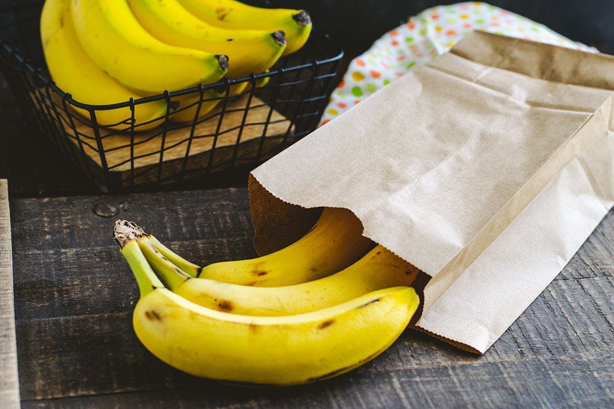 Bananas poking out of a brown paper bag sitting on top of a wooden table.