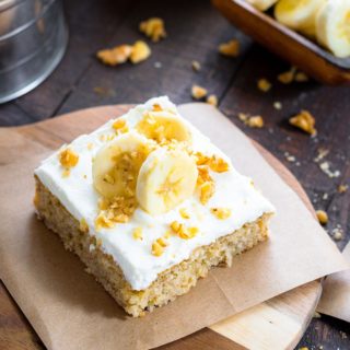 A slice of banana cake on a plate, with sliced bananas and nuts on top.