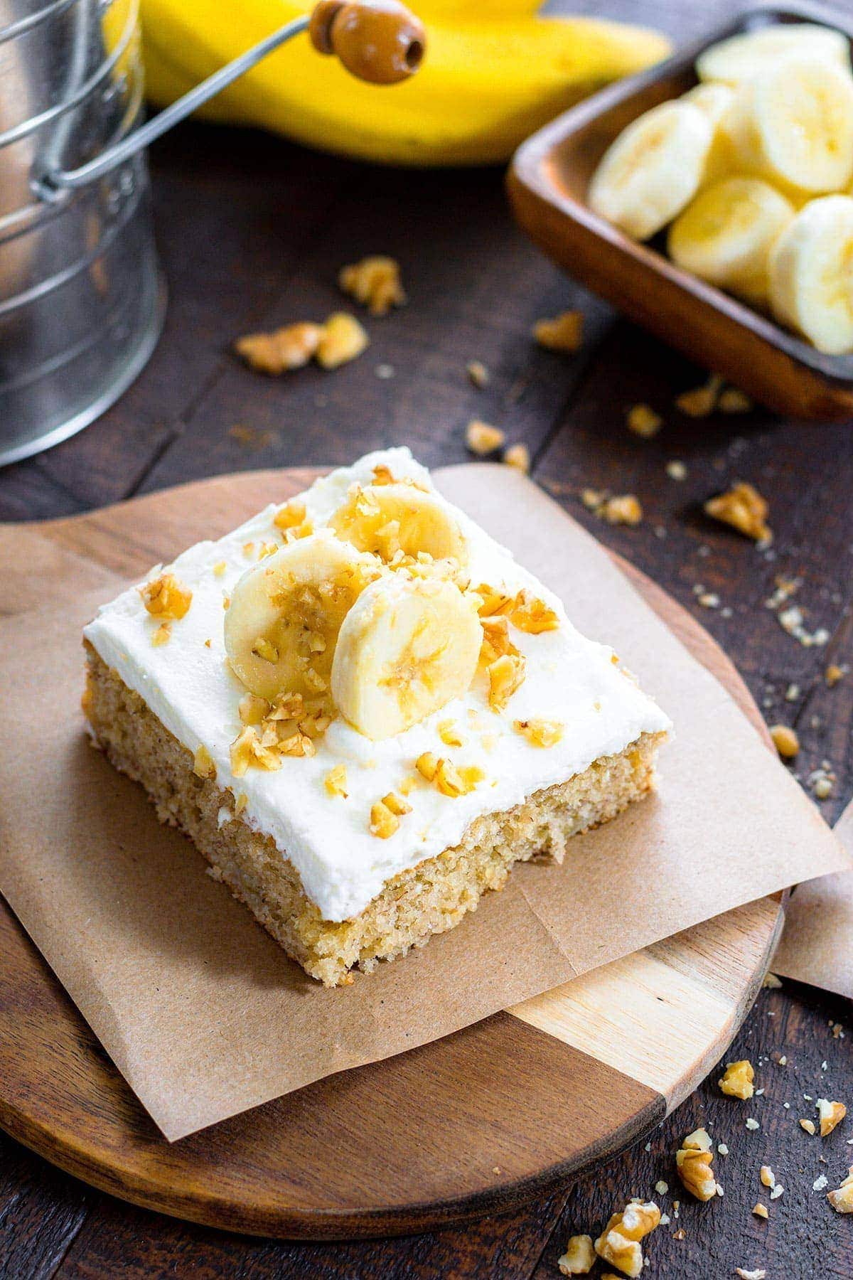 A slice of banana cake on a plate, with sliced bananas and nuts on top.