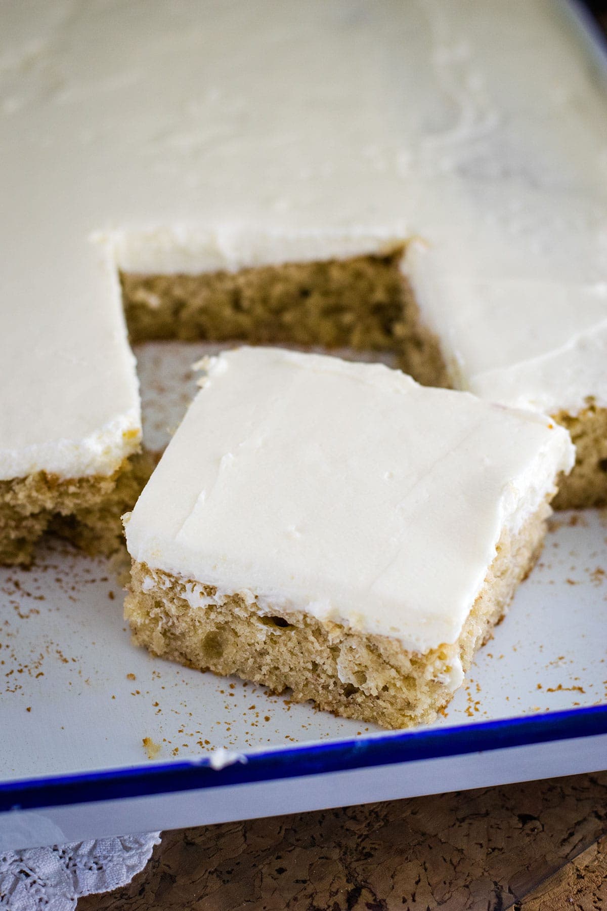 Banana sheet cake slice on a white enamel cake pan with blue trim.