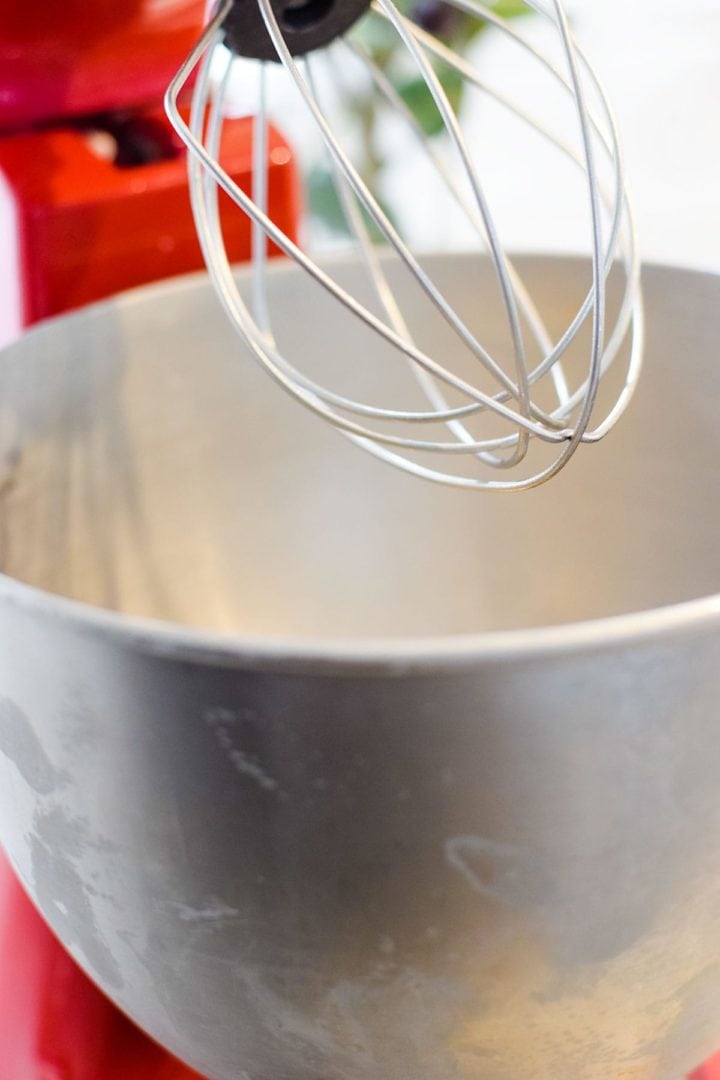 A red stand mixer with a chilled bowl and whisk.