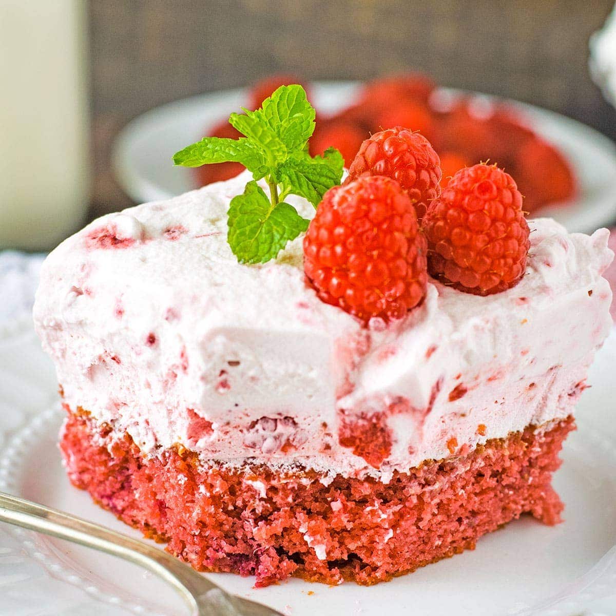 A slice of raspberry fluff cake topped with raspberries and mint leaves.