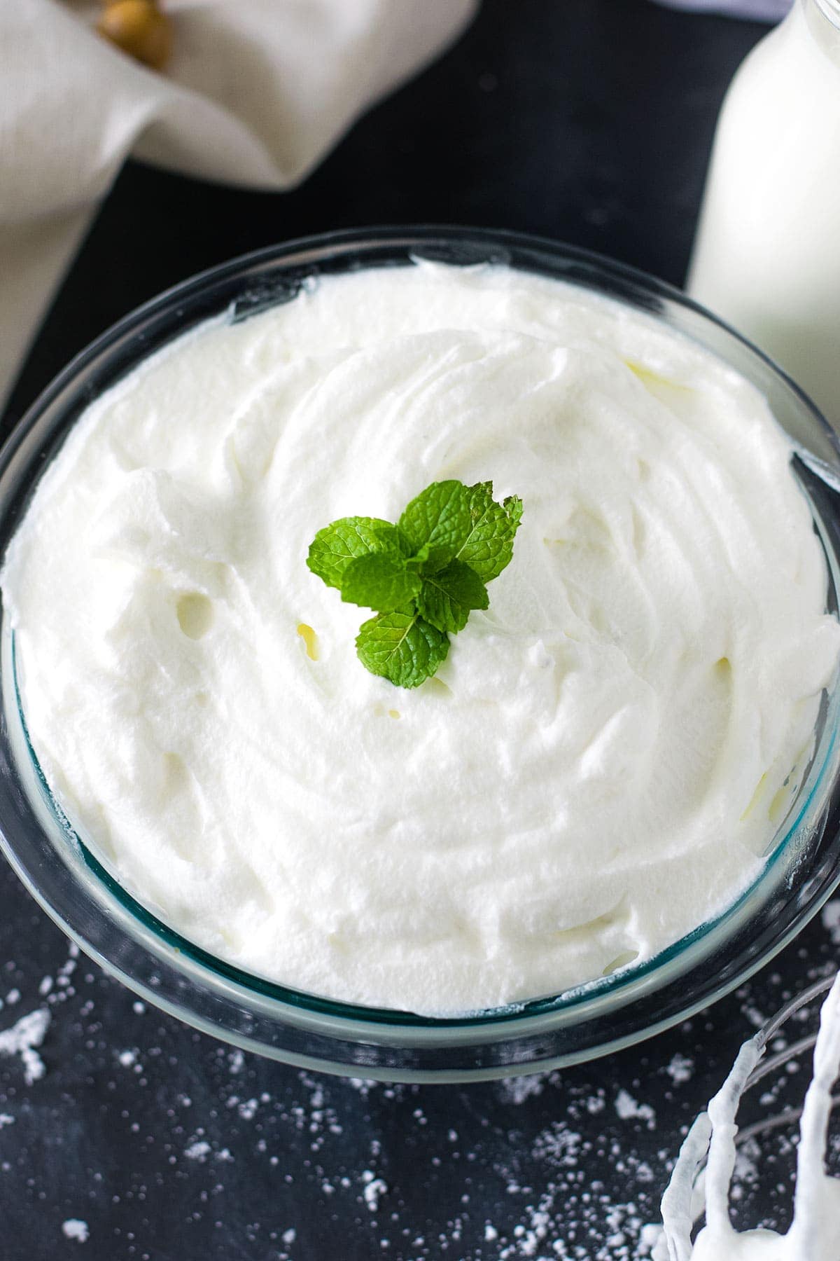 Glass bowl filled with homemade whipped cream garnished with mint leaves.