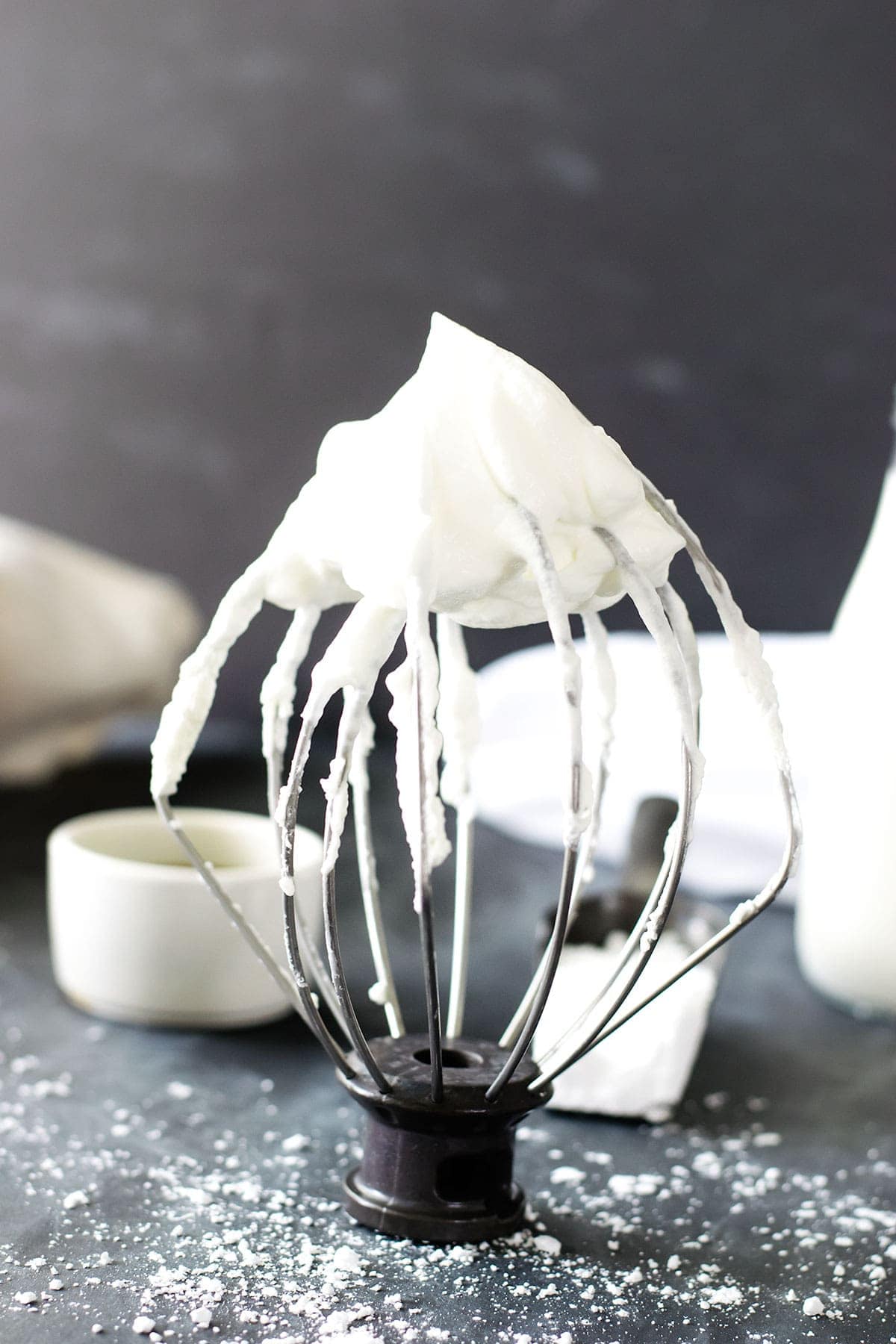 A stand mixer whisk with fluffy whipped cream on top.