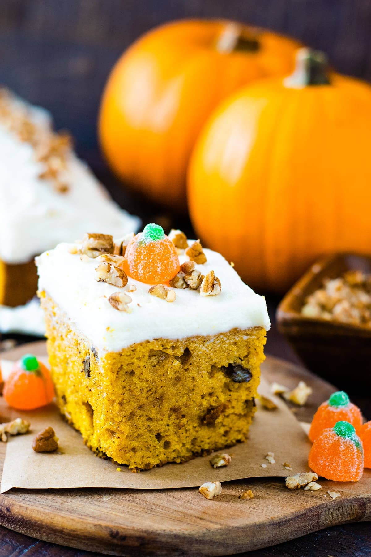 Slice of pumpkin spice cake with orange pie pumpkins displayed in the background.