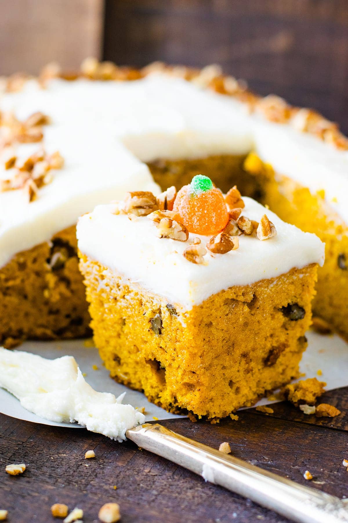 Slice of Pumpkin Spice Cake sprinkled with pecans and a candy pumpkin on a serving board.