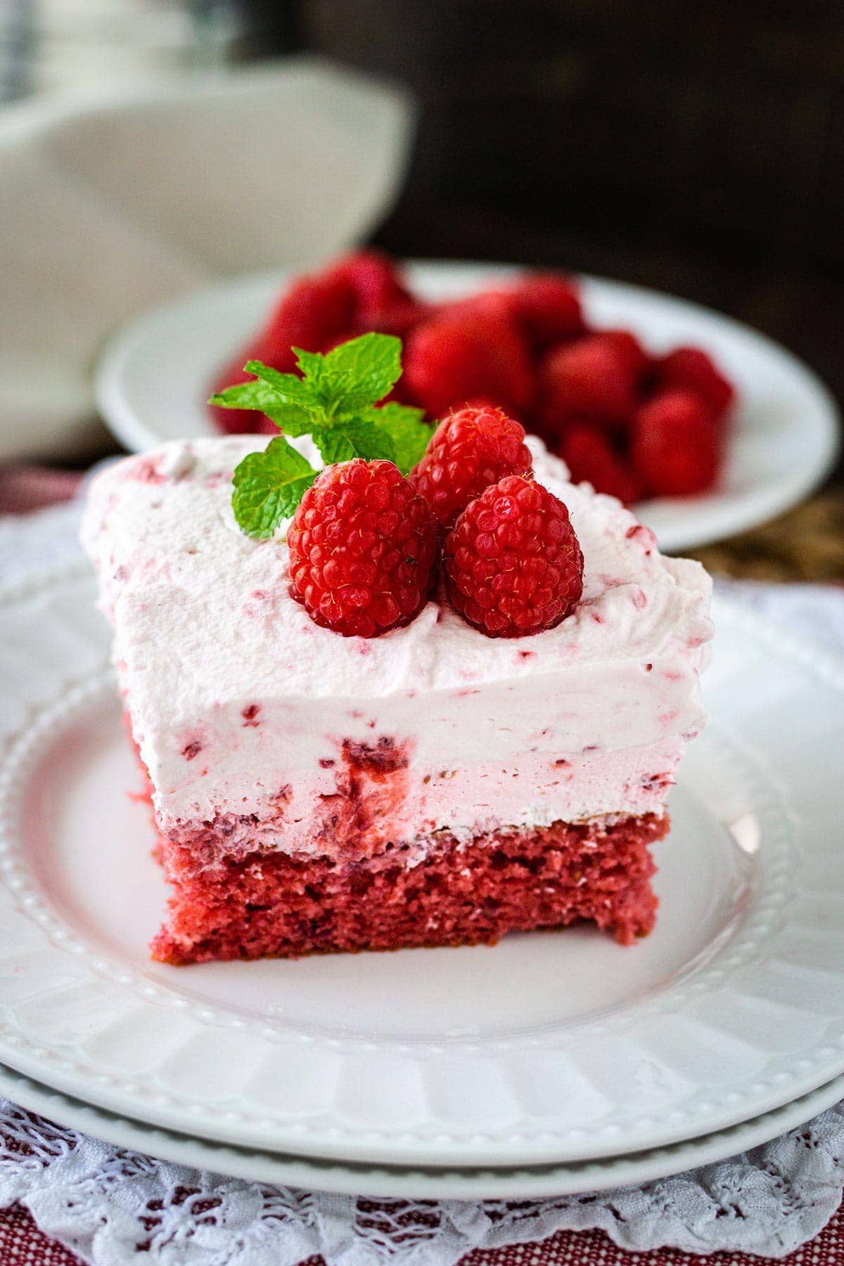 A piece of raspberry fluff cake on a plate topped with fresh raspberries and mint.
