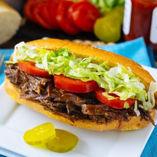 Roast Beef Debris Po Boy on a white plate with pickles.