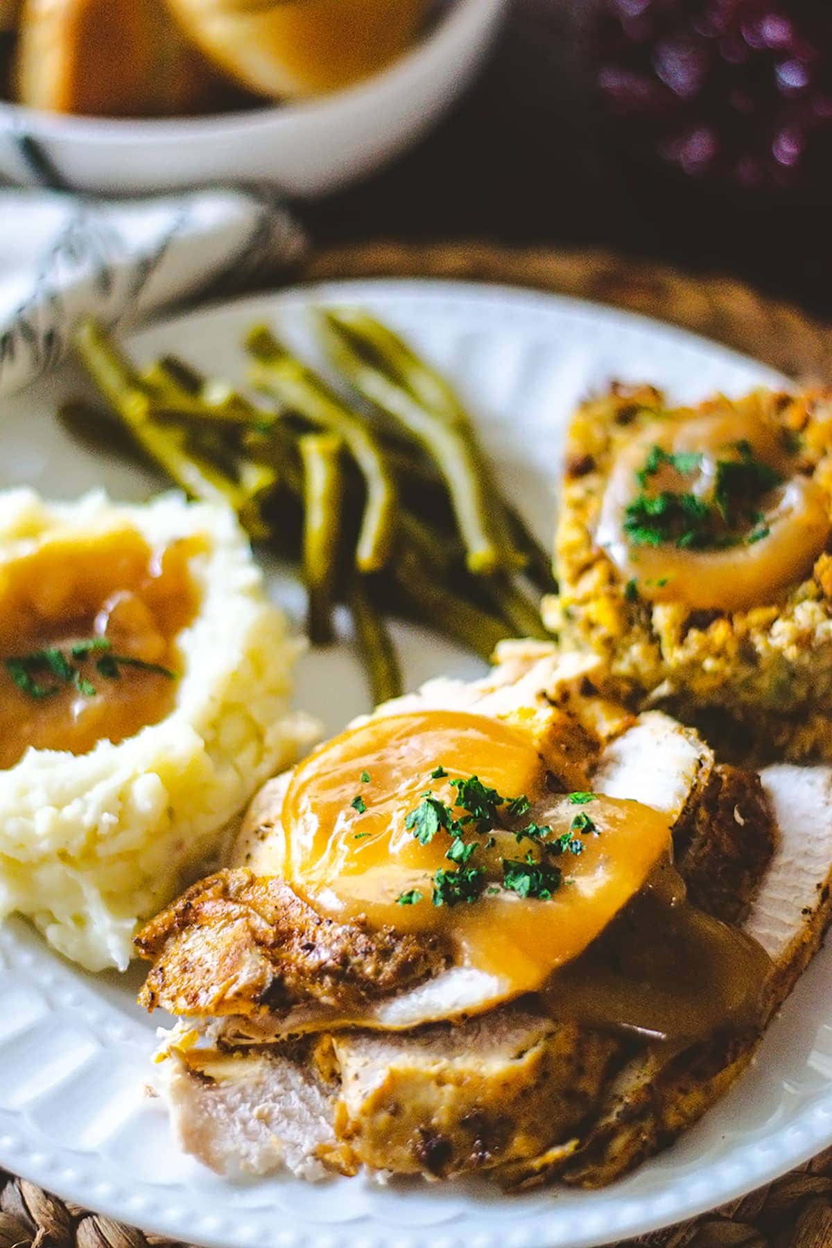 Turkey dinner plated with sliced turkey and gravy, mashed potatoes, green beans and dressing.