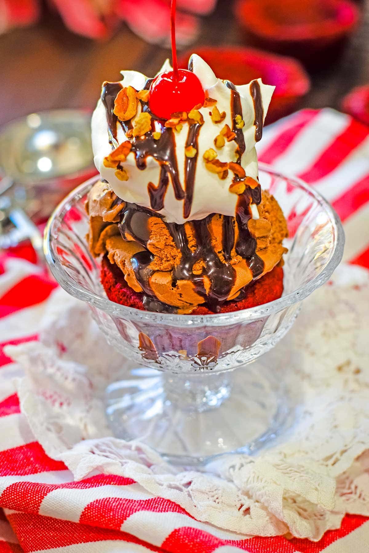 Red Velvet Brownie Cup sundae with chocolate ice cream, a dollop of whipped cream and drizzle of chocolate syrup and topped off with pecans and a cherry. 