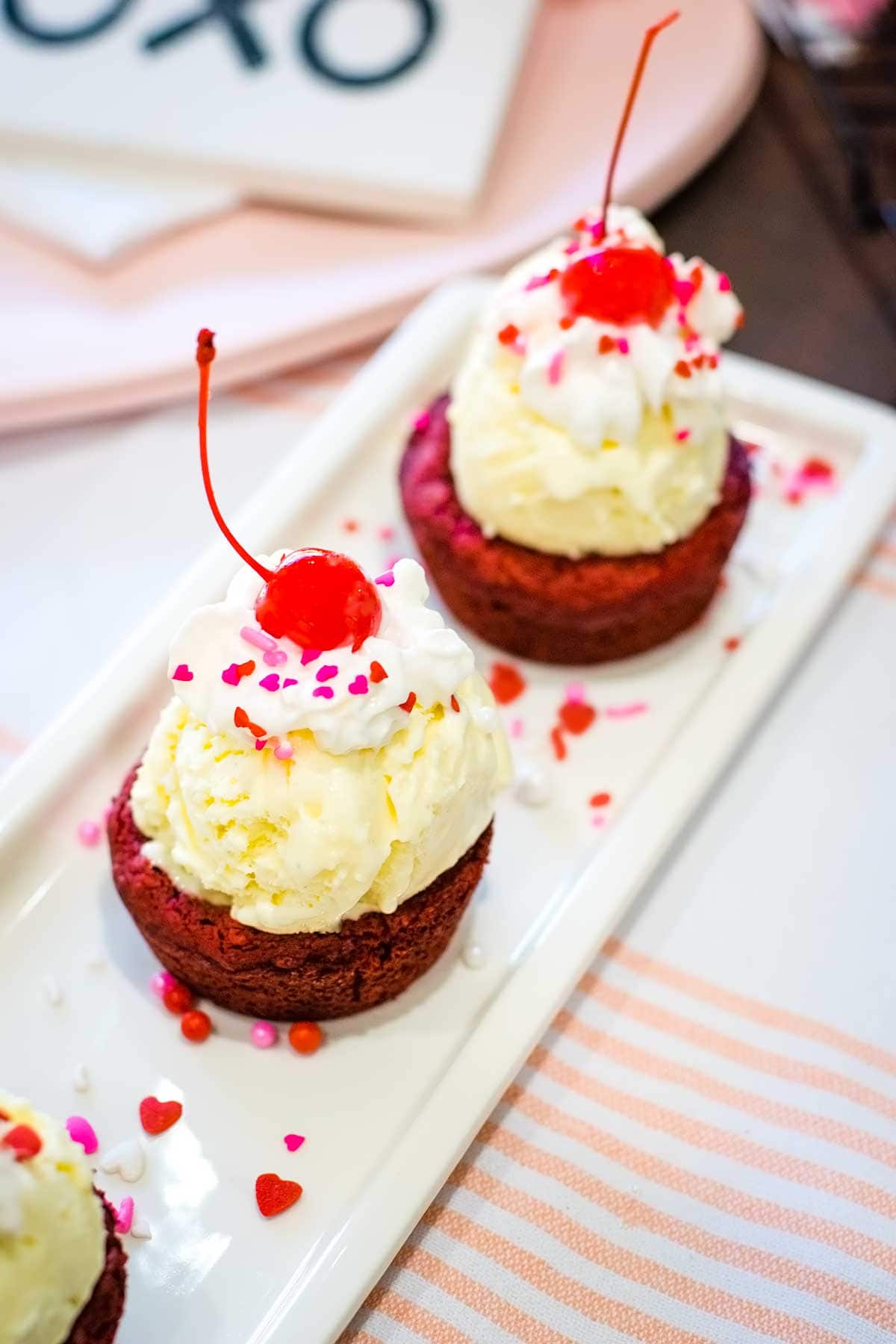 Red Velvet Brownie cups with vanilla ice cream and whipped cream topped with heart sprinkles making them the perfect Valentine's Day dessert.