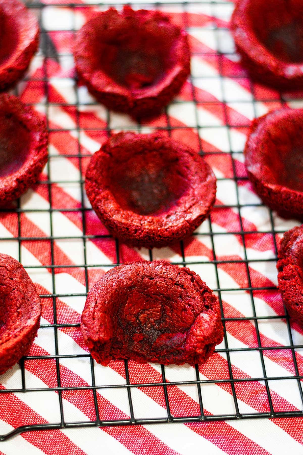 Red Velvet Brownie Cups on a cooling rack with a white and red striped tea towel underneath.