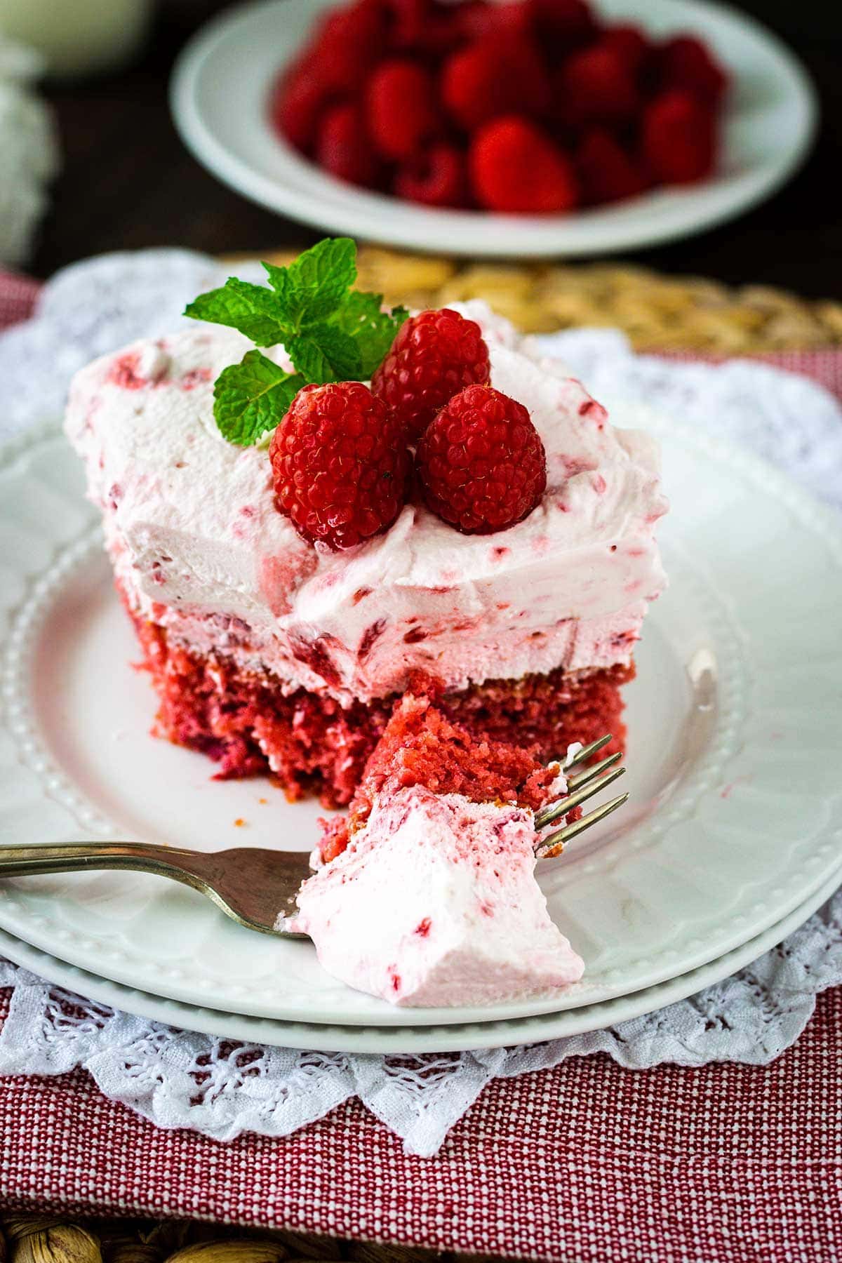Raspberry fluff cake on a white plate with a bite on a fork. 