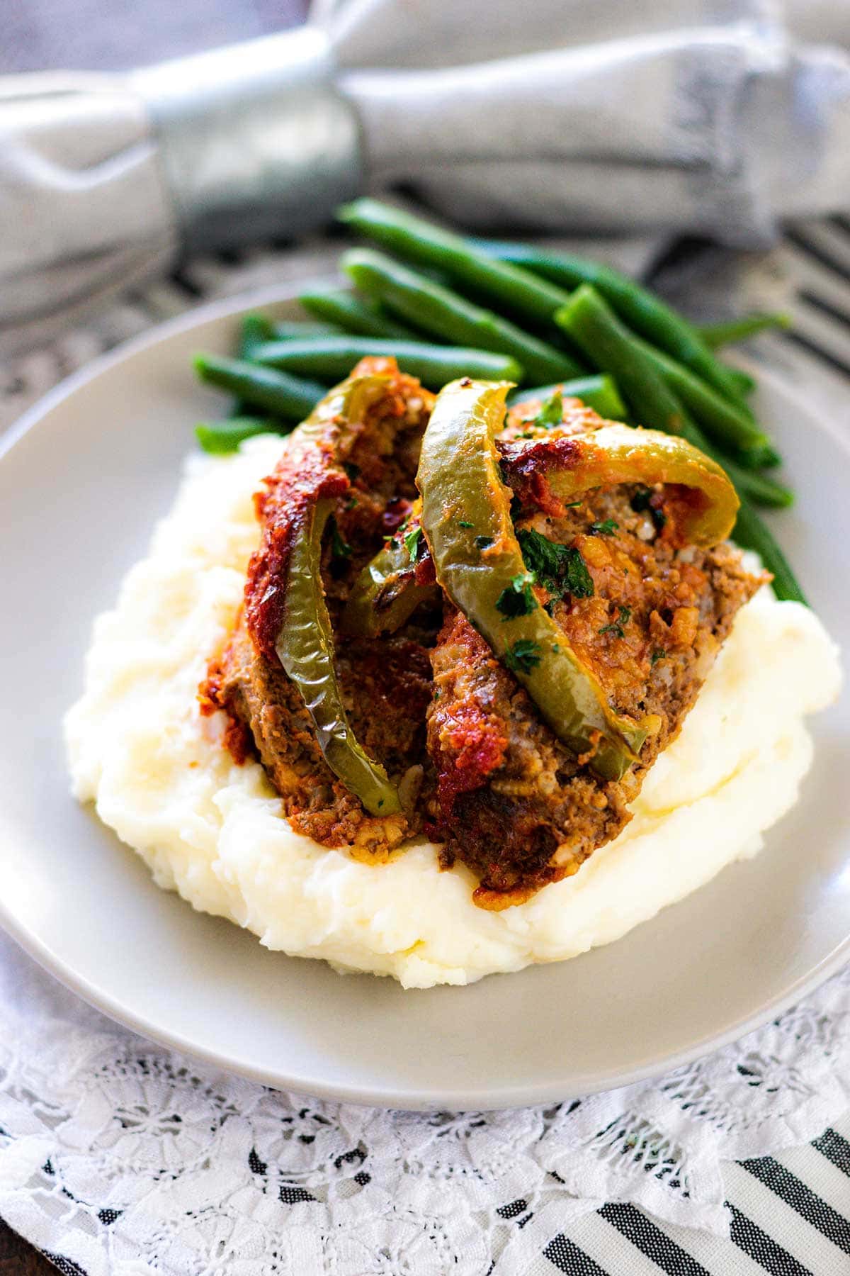 Meatloaf with all the flavors of stuffed peppers on top of mashed potatoes and a side of green beans.