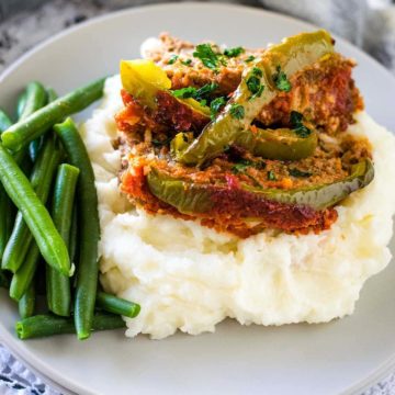 A plate stuffed pepper meatloaf over mashed potatoes served with fresh green beans.