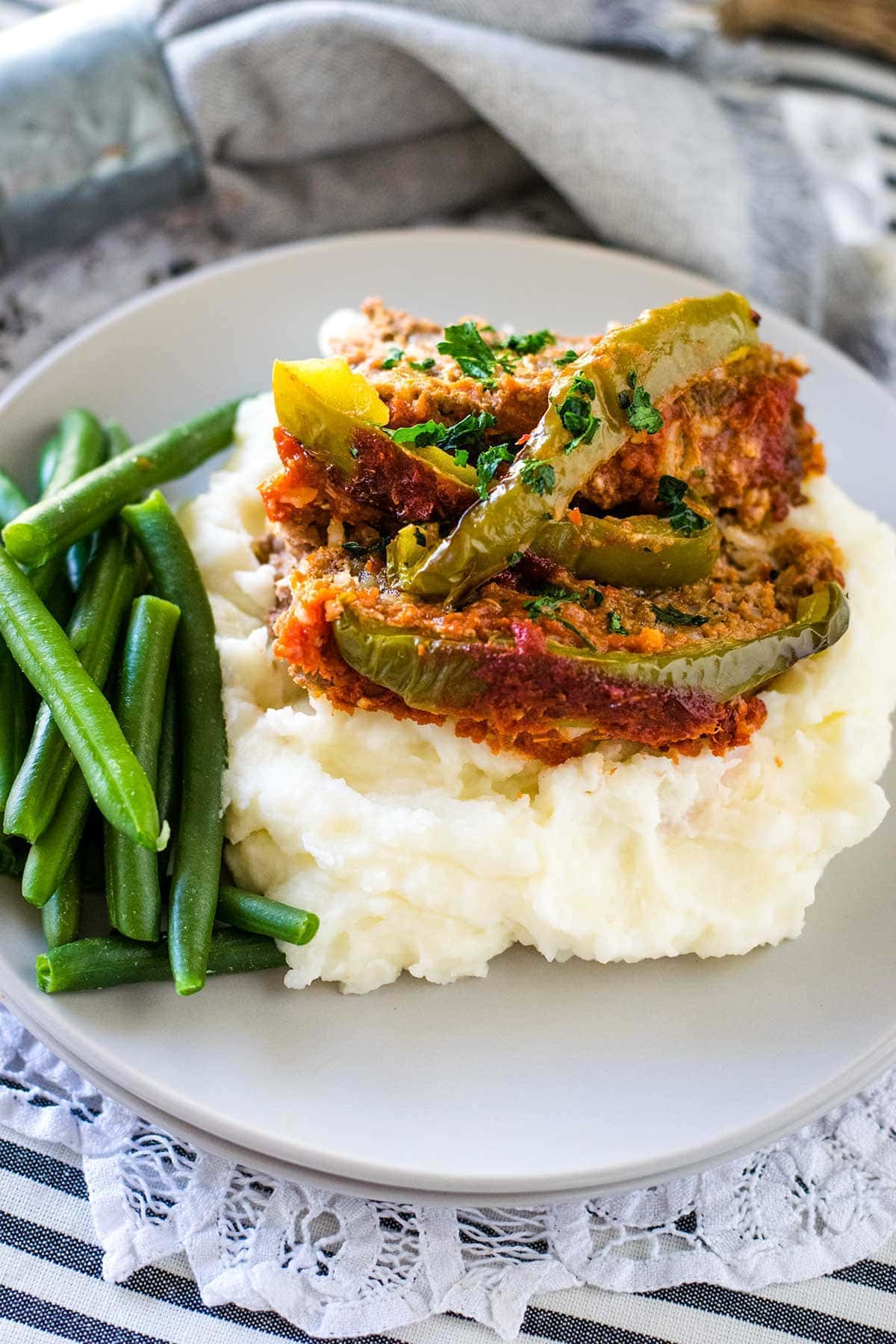 A plate stuffed pepper meatloaf over mashed potatoes served with fresh green beans.