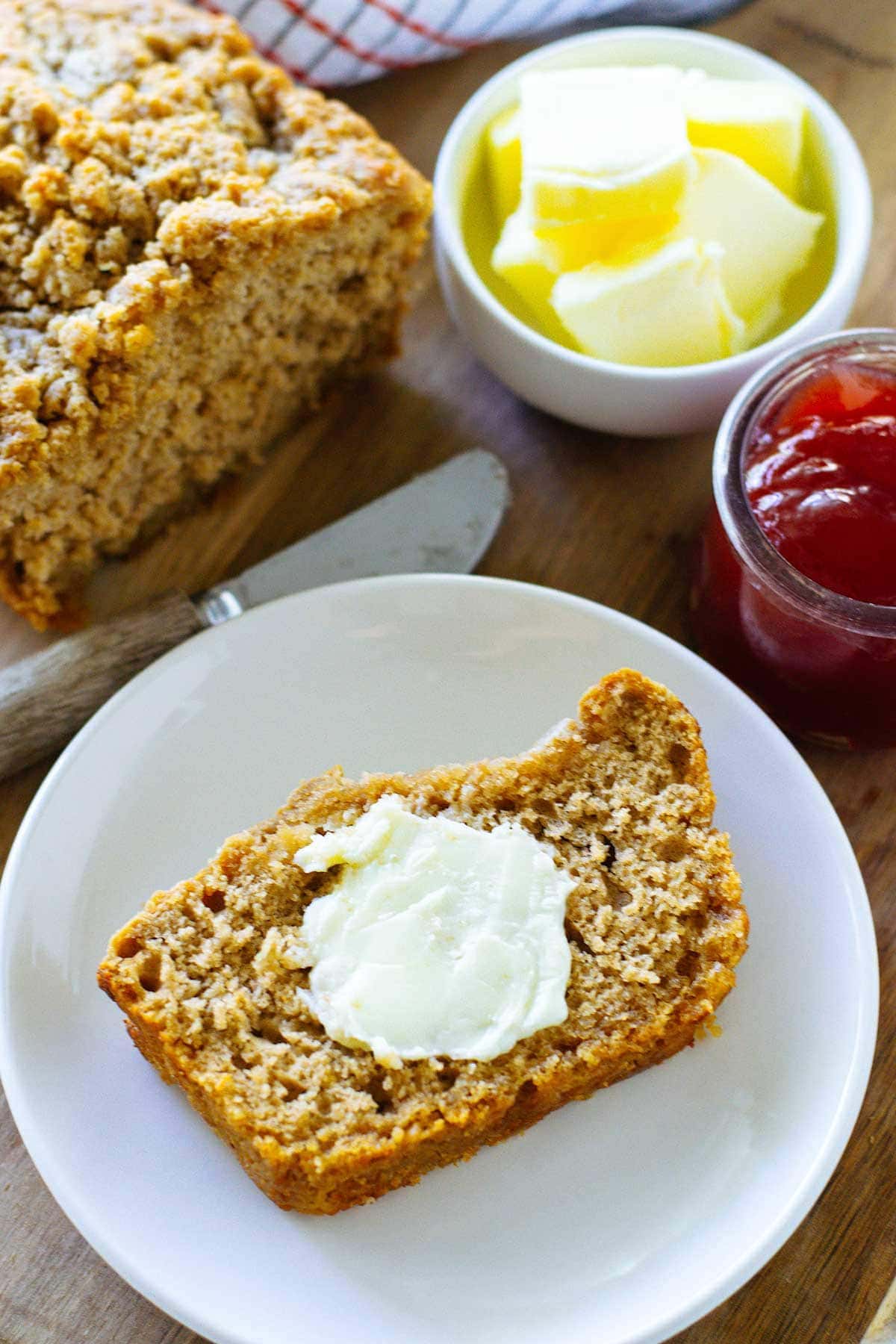 Slice of buttery beer bread with a pat of butter on a serving tray with jam and butter in the background.